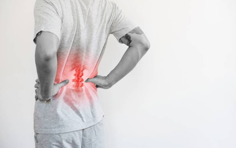 Young man standing with tattoos on his arms while holding his hips with an x ray view of his spine in a bright red color.