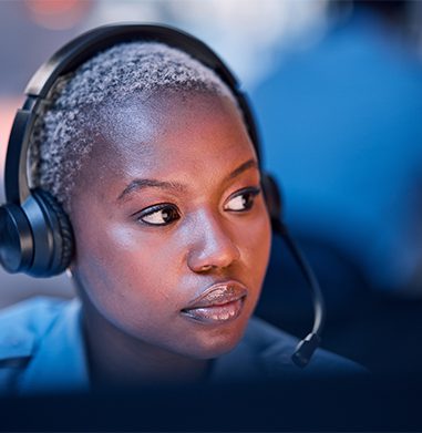 woman sitting at a desk wearing a headset. you can see the computer light reflecting off of her face