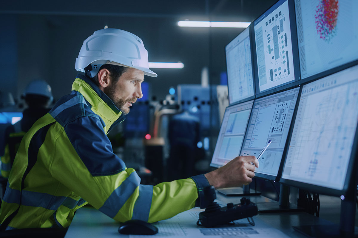 Man in reflective jacket and hard hat reviewing data on computer screens