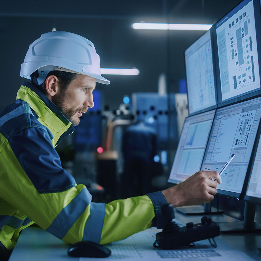 Man in reflective jacket and hard hat reviewing data on computer screens